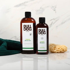 The Premium Body Care Bundle, featuring shower gel and shampoo, is shown on a white surface with a natural sponge and dark green towel against a white marble background.