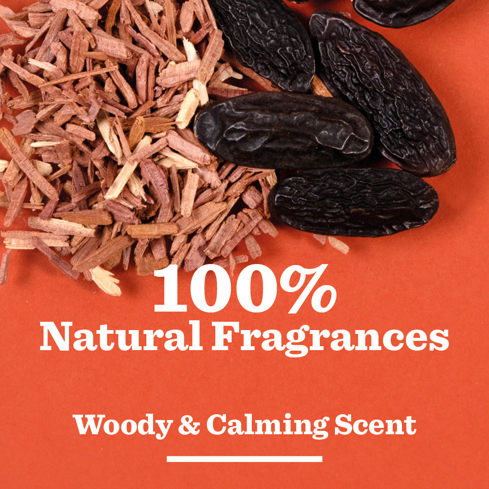 A close-up of shredded woody material and dark pods on an orange background with the text: 100% Natural Fragrances. Cedarwood & Tonka Bean Shower Gel delivers a calming, woody scent.