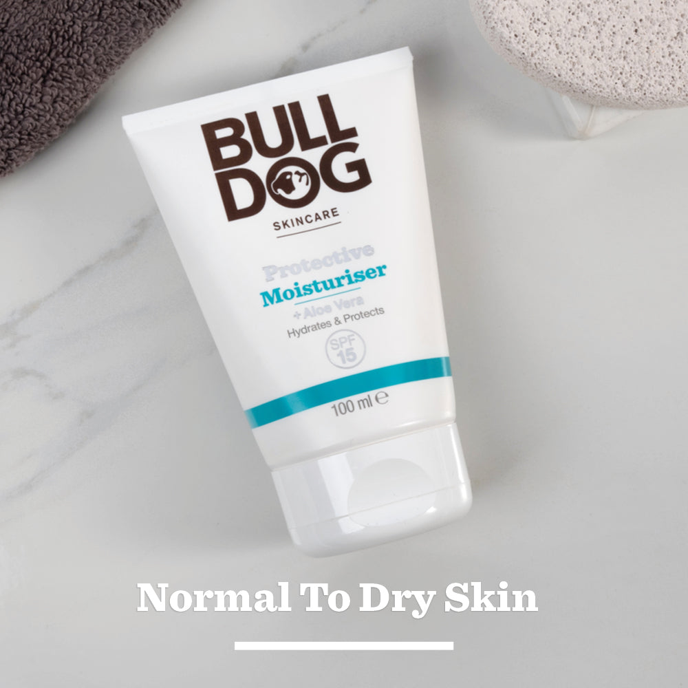 A tube of Protective Moisturiser with SPF 15 is on a light surface beside a textured stone and brown towel. The phrase Normal To Dry Skin appears below the moisturiser.