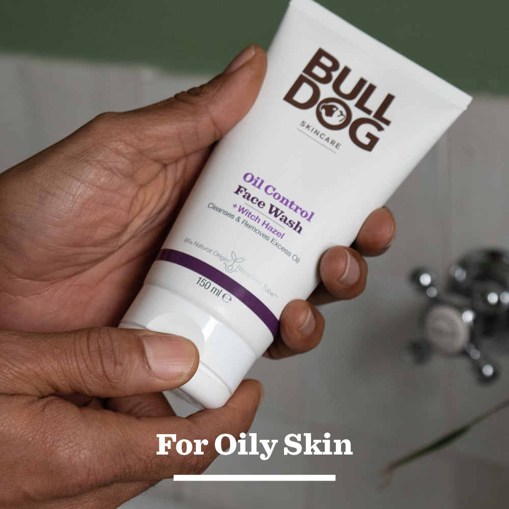 A person holds a tube of Oil Control Face Wash with witch hazel and natural origin ingredients. For Oily Skin is displayed at the bottom, set against a bathroom background.