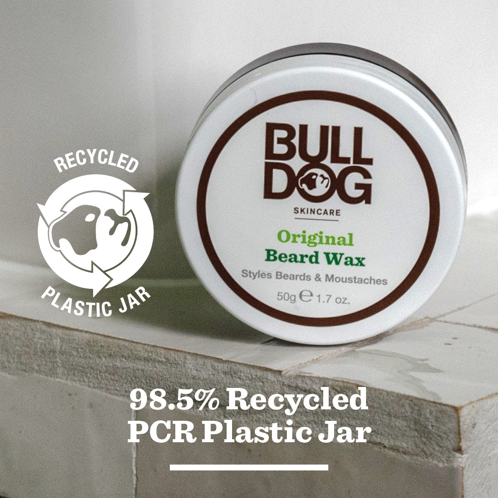 A round container of Original Beard Wax rests on a white surface. The label notes its moisturising formula for beards and moustaches, with natural origin ingredients and a jar made from 98.5% recycled PCR plastic. A recycled plastic icon is shown nearby.